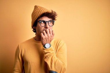 Rahat tişört ve gözlük takan genç yakışıklı adam izole edilmiş sarı arka planda gergin ve gergin görünüyor ve elleri ağızdan tırnak yiyor. Endişe sorunu.