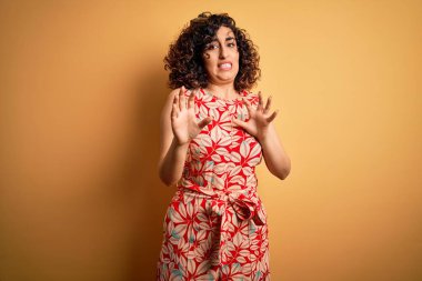 Genç, güzel, kıvırcık Arap kadın tatilde. Çiçekli bir elbise giyiyor ve güneş gözlüğü takıyor. Tiksindirici tepki verdiği için rahatsız ve korku dolu bir ifade takınıyor. Eller havada