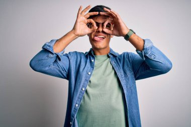 Genç yakışıklı bir adam, gözlüklü, sıradan bir gömlek ve gözlüklü, izole edilmiş beyaz arka planda dürbün gibi güzel hareketler yapıyor. Dürbün gibi dilini dışarı çıkarıyor, gözler parmaklarından bakıyor. Çılgın ifade.