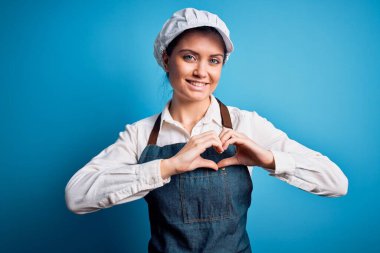 Mavi gözlü, mavi önlüklü, mavi arkaplanlı, güzel fırıncı kadın. Aşkla gülümseyen ve elleriyle kalp sembolü gösteren. Romantik konsept.
