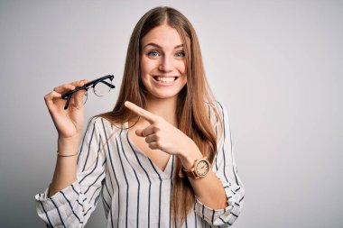 Genç, güzel, kızıl saçlı, optik kadın, izole edilmiş beyaz arka planda gözlük tutuyor.