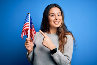 Genç, güzel, vatansever kadın elinde Amerikan bayrağı tutarak 4 Temmuz 'u mutlu bir şekilde el ve parmak göstererek kutluyor.
