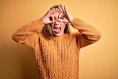 Sarı arka plan üzerinde sıradan bir süveter giyen genç ve güzel bir kadın. Dürbün gibi güzel hareketler yapıyor. Dürbünü dışarı çıkarıyor, gözleri parmaklarından bakıyor. Çılgın ifade.