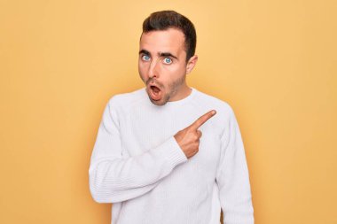 Sarı arka planda dikilen mavi gözlü, genç ve yakışıklı bir adam. Parmakla işaret ederek şaşırmış, ağzı açık, şaşkın bir ifade..