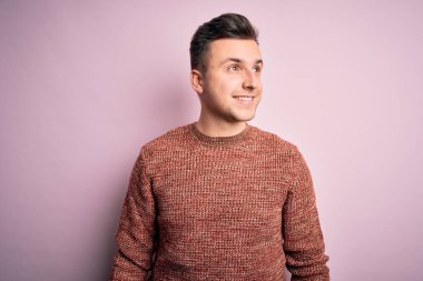 Pembe izole arka plan üzerine günlük kazak giyen yakışıklı beyaz bir adam yüzünde gülümsemeyle, doğal bir ifadeyle yan yana bakıyor. Kendinden emin gülen.