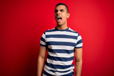 Yakışıklı Afro-Amerikan erkeği, sıradan çizgili tişörtler giymiş, kırmızı arka planda öfkeli ve sinirli bir şekilde bağırıyor, öfkeyle bağırıyor. Öfke ve agresif kavram.