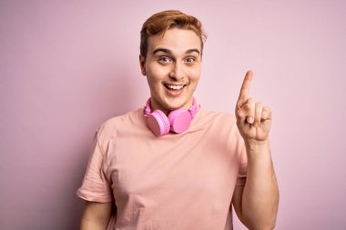 Genç, yakışıklı, kızıl saçlı, müzik dinleyen, pembe arka planda kulaklık takan başarılı bir fikri işaret eden bir adam. Heyecanlı ve mutlu. Bir numara..