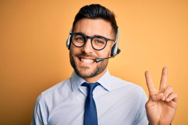 Çağrı merkezinden gelen müşteri hizmetleri kulaklığı takan genç bir işletmeci kameraya gülümseyen bir gülümsemeyle zafer işareti yapıyor. İki numara..