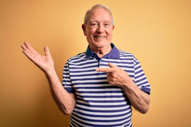 Gri saçlı, donanma çizgili tişört giyen son sınıf öğrencisi sarı arka planda durup kameraya hayret ediyor ve gülümsüyor..