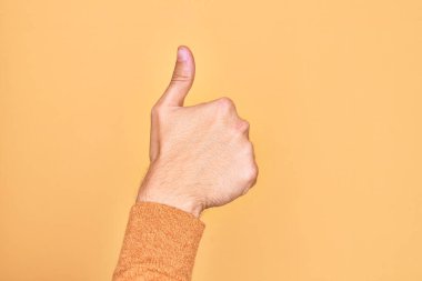 İzole edilmiş sarı arka plan üzerinde parmaklarını gösteren beyaz bir gencin eli başarılı bir onay jesti yapıyor. Başparmak işareti, onaylama ve olumlu sembol ile.