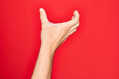 Kafkasyalı genç adam parmaklarını izole edilmiş kırmızı arka planda gösteriyor. Elinde görünmez bir nesne var. Elleri boş ve kırpma hareketi yapıyor.