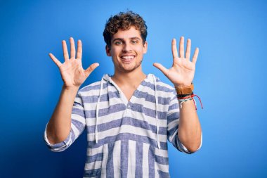 Sarışın, kıvırcık saçlı, sıradan çizgili kazak giyen, on numarayı gösteren ve gülümseyen, kendinden emin ve mutlu genç bir adam..