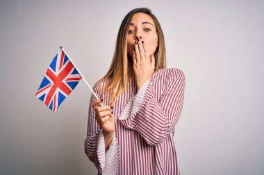 Mavi gözlü, genç, sarışın bir kadın Birleşik Krallık bayrağını tutuyor. Ağzı ve ağzı kapalı. Yanlışlıkla şok olmuş, korku ifadesi, sessizlikten korkmak, gizli bir kavram.