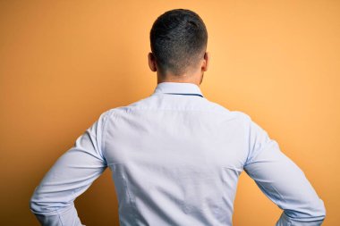 Sarı arka planda duran kravat ve gözlük takan genç yakışıklı işadamı kolları vücudunda geriye doğru bakıyor.