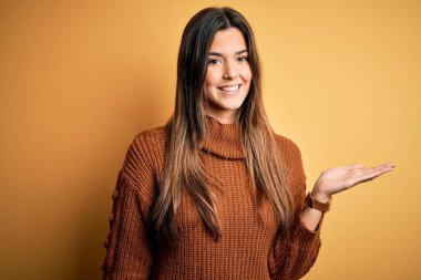 İzole edilmiş sarı arka planda dikilen sıradan bir süveter giyen genç ve güzel bir kız. Gülümsüyor, avucunun içi gibi kameraya bakıyor..