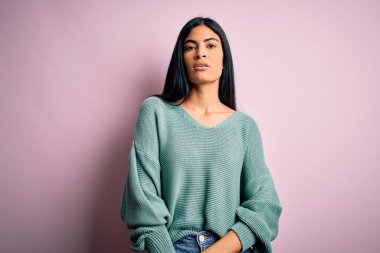 Pembe arka planda yeşil süveter giyen, yüzünde ciddi bir ifade olan genç ve güzel İspanyol moda kadını. Basit ve doğal bir şekilde kameraya bakıyorsun..