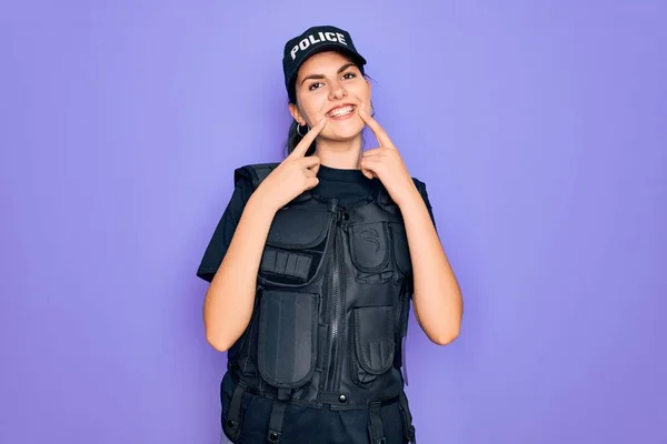 Young police woman wearing security bulletproof vest uniform over purple background Smiling with open mouth, fingers pointing and forcing cheerful smile