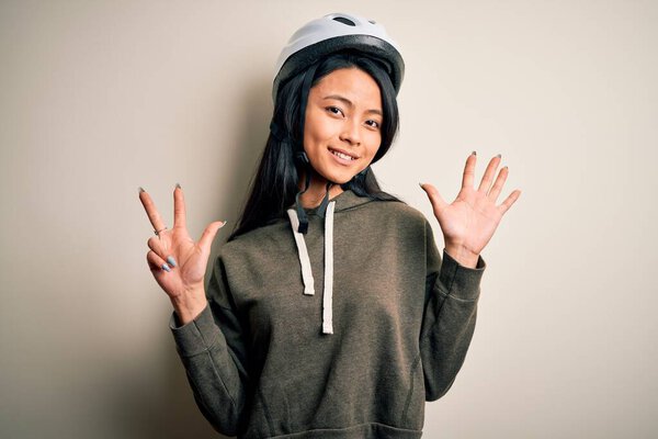 Young beautiful chinese woman wearing bike helmet over isolated white background showing and pointing up with fingers number eight while smiling confident and happy.