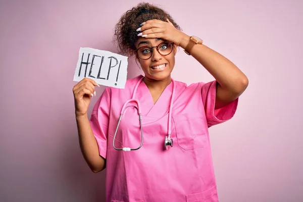 stock image African american doctor girl wearing medical uniform and stethoscope holding help paper stressed with hand on head, shocked with shame and surprise face, angry and frustrated. Fear and upset for mistake.