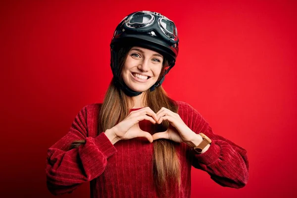 赤い背景の上に元のヘルメットをかぶっている若い美しい赤毛の元サイクリストの女性は ハートのシンボルと手で形を示す愛に笑みを浮かべています ロマン主義 — ストック写真