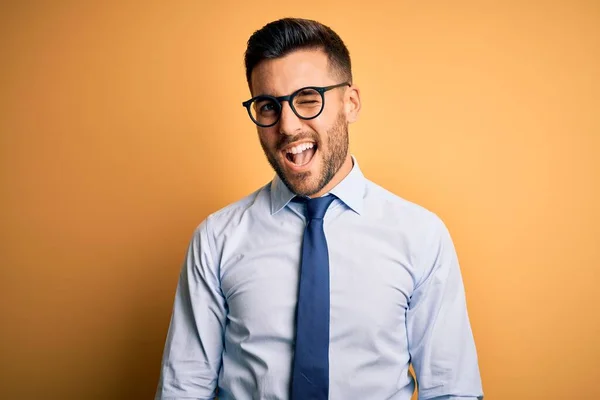 若いですハンサムなビジネスマン身に着けているネクタイと眼鏡上の黄色の背景ウィンク見ますザ カメラとともにセクシー式 陽気で幸せな顔 — ストック写真