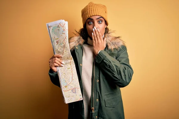 African american skier tourist girl wearing snow sportswear and ski goggles holding city map cover mouth with hand shocked with shame for mistake, expression of fear, scared in silence, secret concept