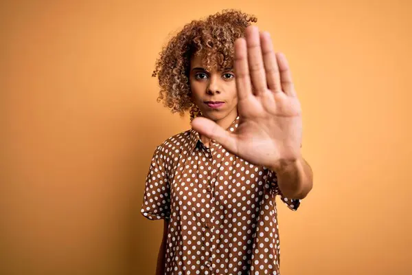黄色の背景の上に立つカジュアルなシャツを着た若い美しいアフリカ系アメリカ人女性は 手の手のひらで歌うのをやめます 顔に負と深刻なジェスチャーで警告式 — ストック写真