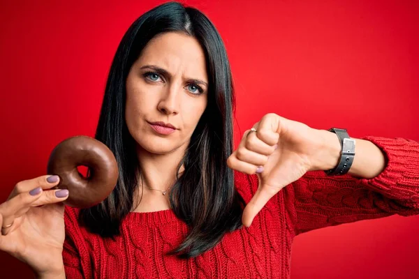 年轻的黑发女人 蓝眼睛 吃巧克力甜甜圈而不是红脸红脸 负面迹象显示不喜欢拇指朝下 拒绝的概念 — 图库照片