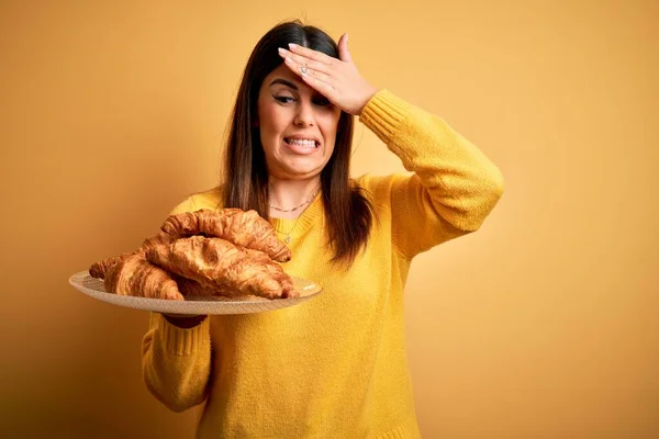 黄色の背景の上にフランスのクロワッサンのペストリーを保持若い美しい女性の頭の上に手で強調し 恥と驚きの顔でショックを受け 怒りと不満 恐怖と過ちへの動揺 — ストック写真