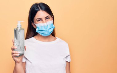 Koronavirüs için koruyucu maske takan genç bir kadın virüs hastalığına karşı el dezenfektanı tutarken pozitif ve mutlu görünüyor.