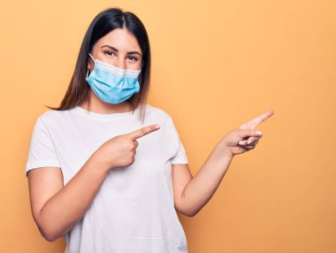 Koronavirüs hastalığı için koruyucu maske takan genç bir kadın sarı arka planda gülümsüyor ve kameraya bakıyor..