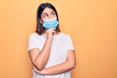 Koronavirüs hastalığı için koruyucu maske takan genç bir kadın sarı arka planda şüpheye odaklanmıştı.