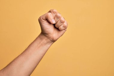 İzole edilmiş sarı arka planda, protesto ve devrim hareketleri yapan, güç ve güç gösterisi yapan beyaz bir gencin eli.