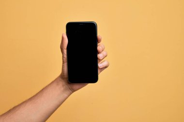 Kafkasyalı genç adam elinde akıllı telefonuyla izole edilmiş sarı arka planda ekranı gösteriyor.