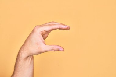 İzole edilmiş sarı arka plan üzerinde parmaklarını gösteren beyaz bir adamın eli. Görünmez bir şeyi alıp, parmaklarıyla uzayı gösteren bir nesneyi tutuyor.