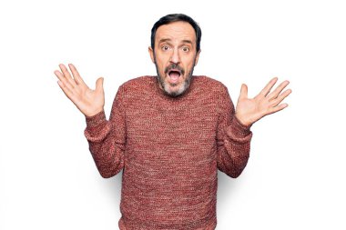 Soyutlanmış beyaz arka plan üzerinde duran, sıradan bir süveter giyen, kolları açık, hiçbir fikri olmayan ve şüpheli bir yüzü olan orta yaşlı yakışıklı bir adam..