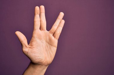Kafkas 'lı genç adam parmaklarını izole edilmiş mor arka planda gösteriyor Vulkan selamı veriyor, el ve parmaklarını gösteriyor, ucube kültürü sergiliyor.