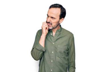 Orta yaşlı, yeşil tişörtlü yakışıklı bir adam izole edilmiş beyaz arka planda şüpheye odaklanmış, çenesinde parmak olan ve kafasını kaldırıp merak eden biri.