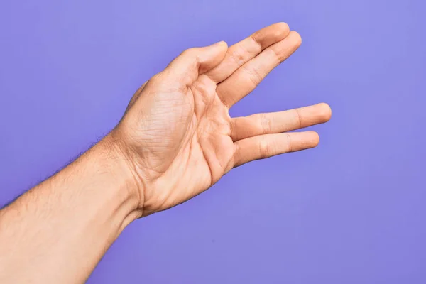 Hand of caucasian young man showing fingers over isolated purple background greeting doing Vulcan salute, showing hand palm and fingers, freak culture