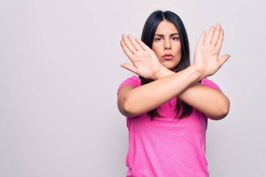 Genç, güzel, esmer, günlük pembe tişört giyen, beyaz arka planda duran, reddedilmiş, kollarını kavuşturan, negatif işaret veren, kızgın yüzlü bir kadın.