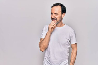 İzole edilmiş beyaz arka plan üzerinde sıradan tişörtler giyen yakışıklı bir adam kameraya kollarını kavuşturmuş ve çenesine dokunmuş bir şekilde gülümsüyor. Olumlu düşünüyorum..