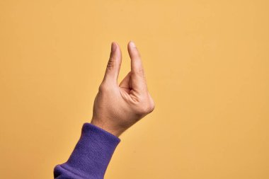 İzole edilmiş sarı arka plan üzerinde parmaklarını gösteren beyaz bir adamın eli. Görünmez bir şeyi alıp, parmaklarıyla uzayı gösteren bir nesneyi tutuyor.