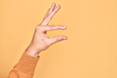 İzole edilmiş sarı arka plan üzerinde parmaklarını gösteren beyaz bir adamın eli. Görünmez bir şeyi alıp, parmaklarıyla uzayı gösteren bir nesneyi tutuyor.