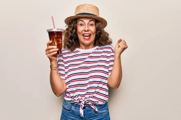 中年黑发女人戴着夏帽 喝着新鲜的可乐 在孤独的背景下尖叫着自豪 高举双臂庆祝胜利和成功 — 图库照片