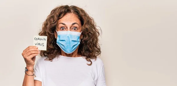 中年女性を身に着けているコロナウイルス保護マスク保持ウイルス病リマインダー紙恐怖と驚きのために口を開けて驚いて 不信顔 — ストック写真