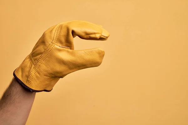 Ręka Białego Młodzieńca Rękawicą Ogrodnika Nad Odizolowanym Żółtym Tłem Zbierająca — Zdjęcie stockowe