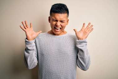 İzole edilmiş beyaz arka plan üzerinde dikilmiş, kollarını kaldırmış ve gözleri kapalı heyecanlı bir şekilde çılgın ve çılgın bir başarıyı kutlayan genç, yakışıklı Latin bir adam. Kazanan konsept