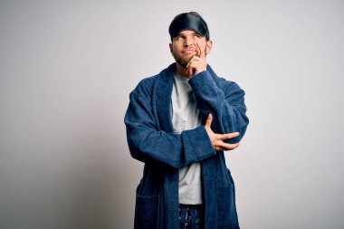 Sakallı, mavi gözlü, uyku maskesi takan ve eli çenesinde pijama giyen soru soran genç sarışın bir adam. Düşünceli bir ifade. Düşünceli bir yüzle gülümsüyor. Şüphe kavramı.