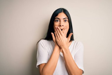 İzole edilmiş arka plan üzerinde gündelik beyaz tişört giyen genç ve güzel İspanyol kadın yanlışlıkla ağızlarını kapatarak şok geçirdi. Gizli konsept.