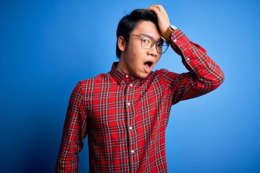 Mavi arka plan üzerine günlük gömlek ve gözlük takan yakışıklı Çinli bir adam hata sonucu el ele tutuşarak şaşırdı. Hatayı unutmayın. Unuttum, kötü hafıza konsepti.